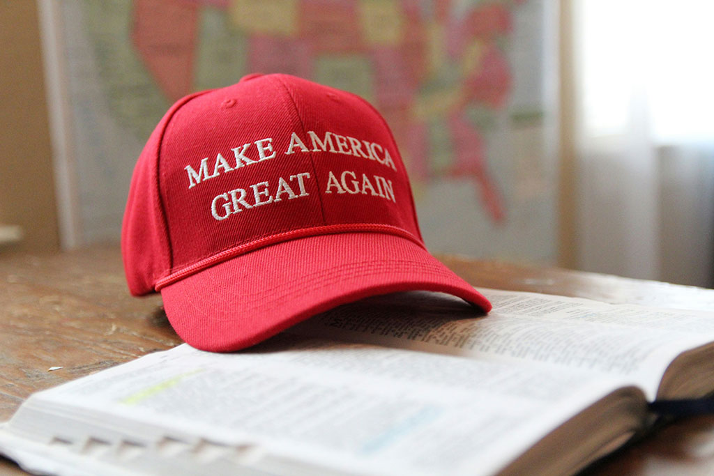 A red baseball cap, with Make America Great Again written across it, sits on an open bible.