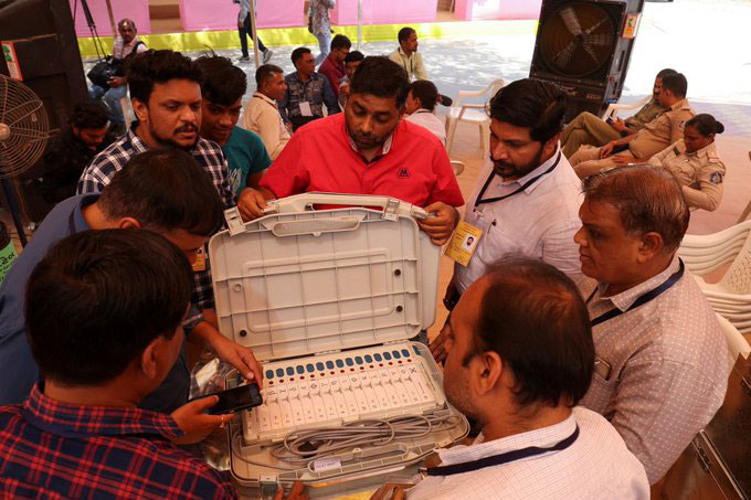 official surround an open case containing an electronic voting terminal and cables.