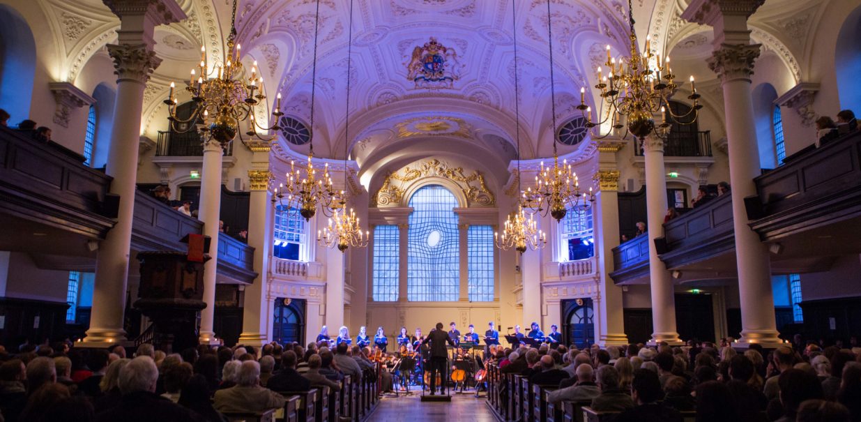 A choir sing at the front of a church while an audience looks on.