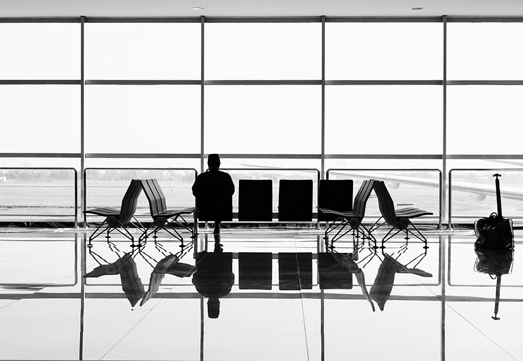 A large airport window silhouettes a bench at which one person sits.