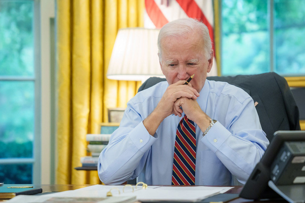 President Biden sits at a desk, holding his balled hands to his mouth.