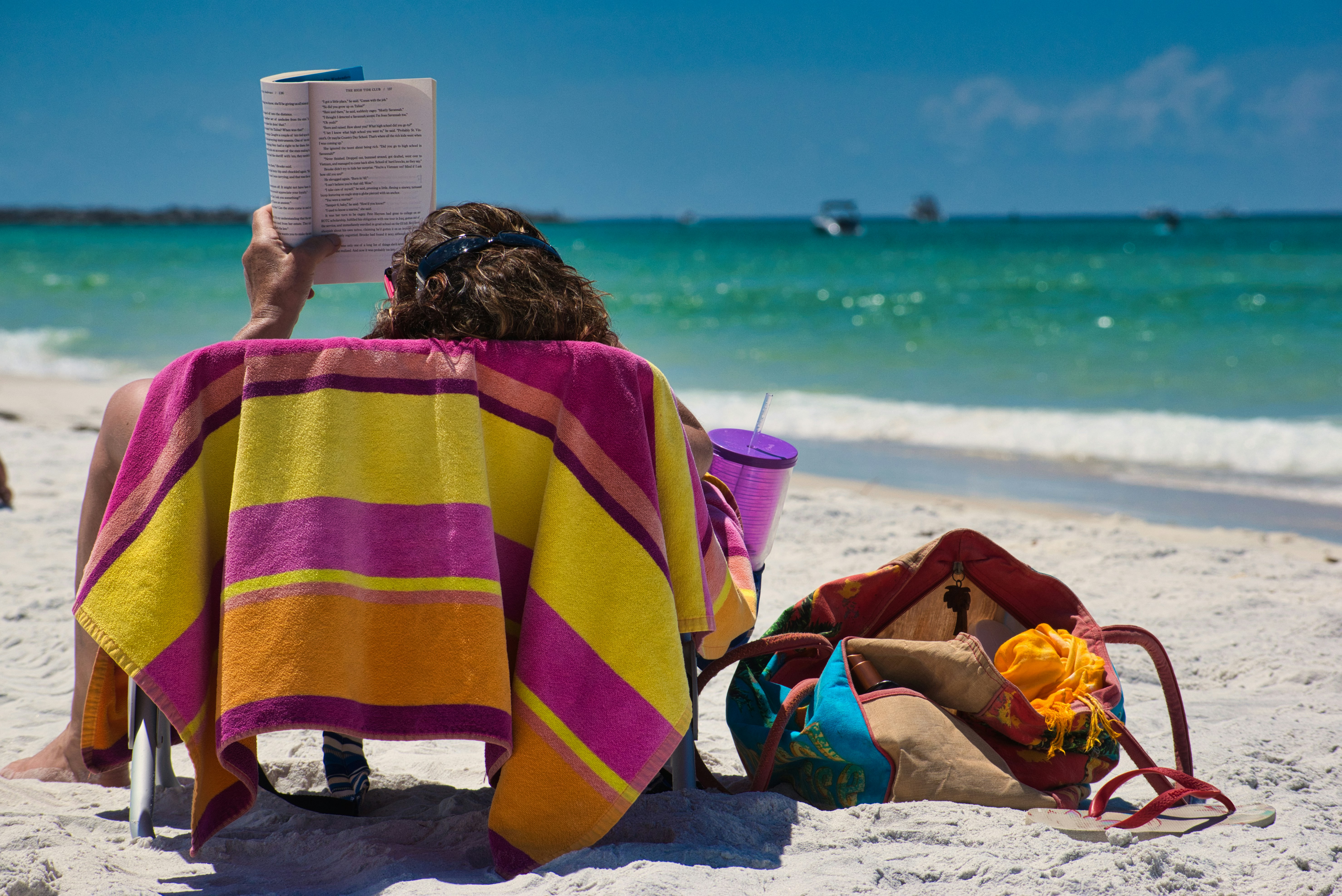 On a beach lounger someone holds a book aloft to read.