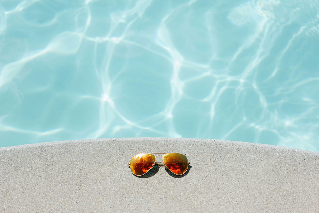 A pair of sunglasses beside a swimming pool.