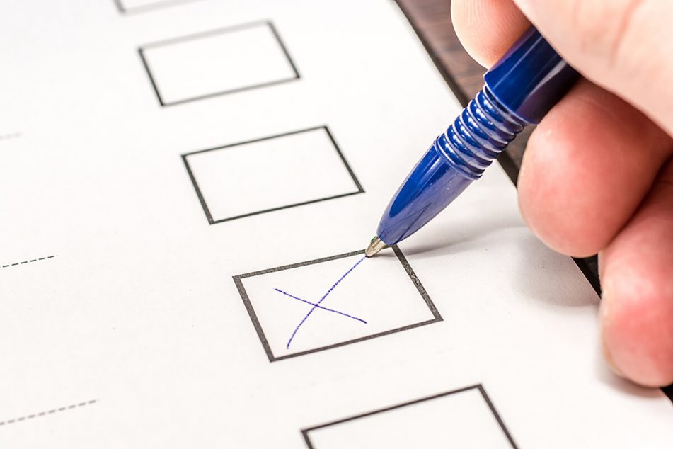 A pen draws a cross in a box on a ballot form.