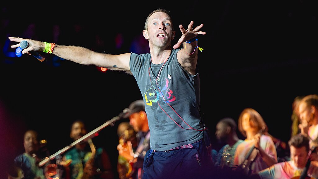 A singer on a stage holds out his arms to conduct the crowd.