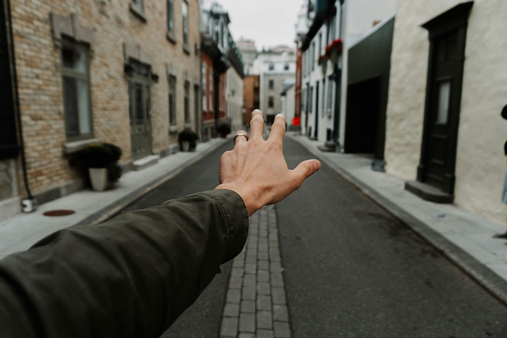 An arm and hand stretch out in front of some, a narrow street is the background.