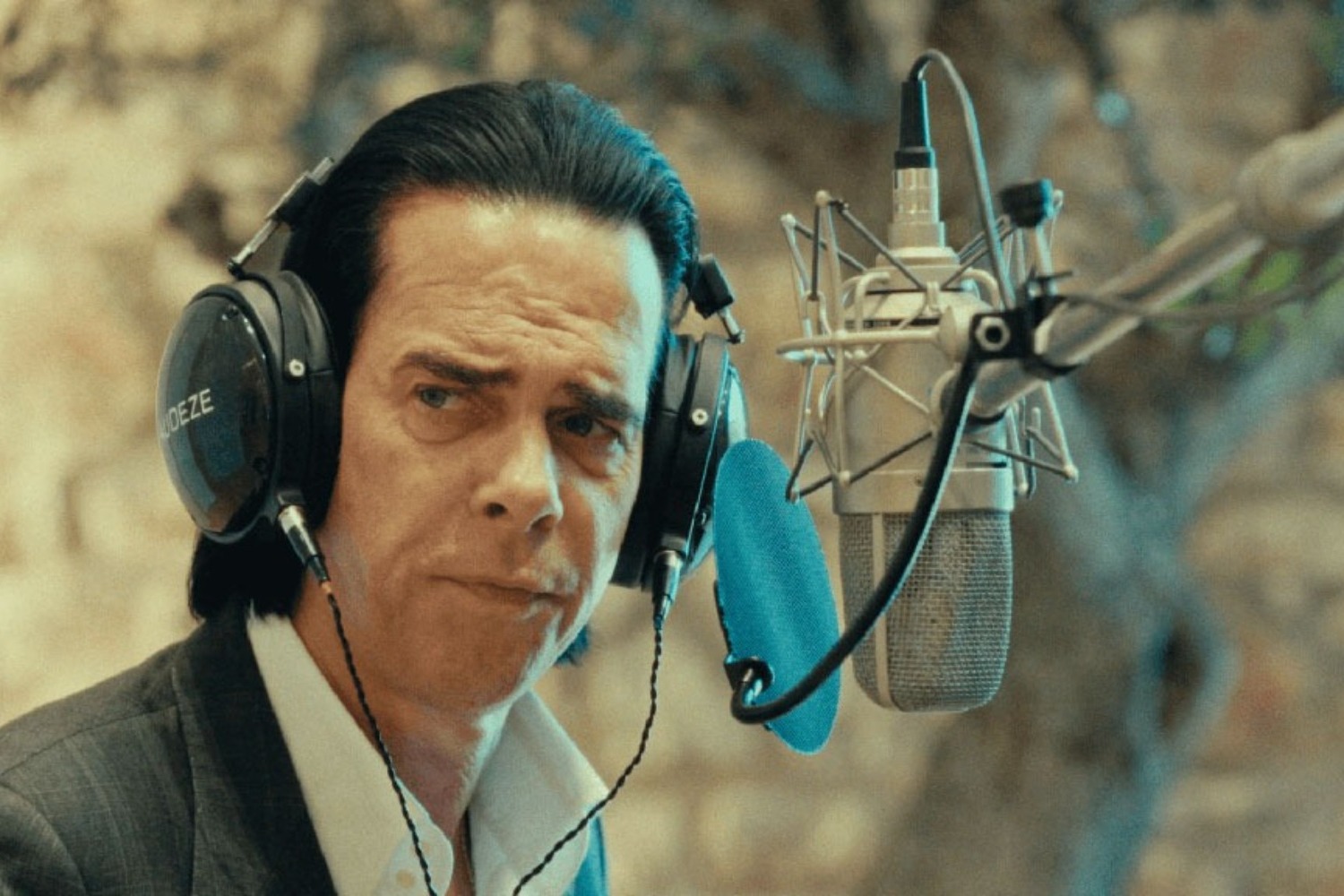 A singer, wearing headphones, turns from a microphone in front of him.
