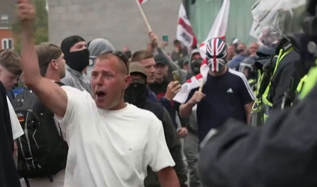 Rioters confront police, one wearing a sinister Union Jack mask
