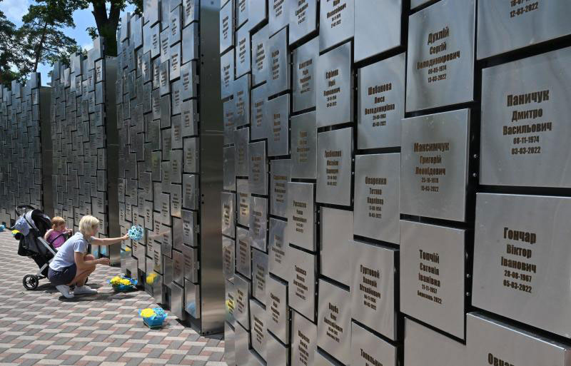 A woman squats and touches a war memorial