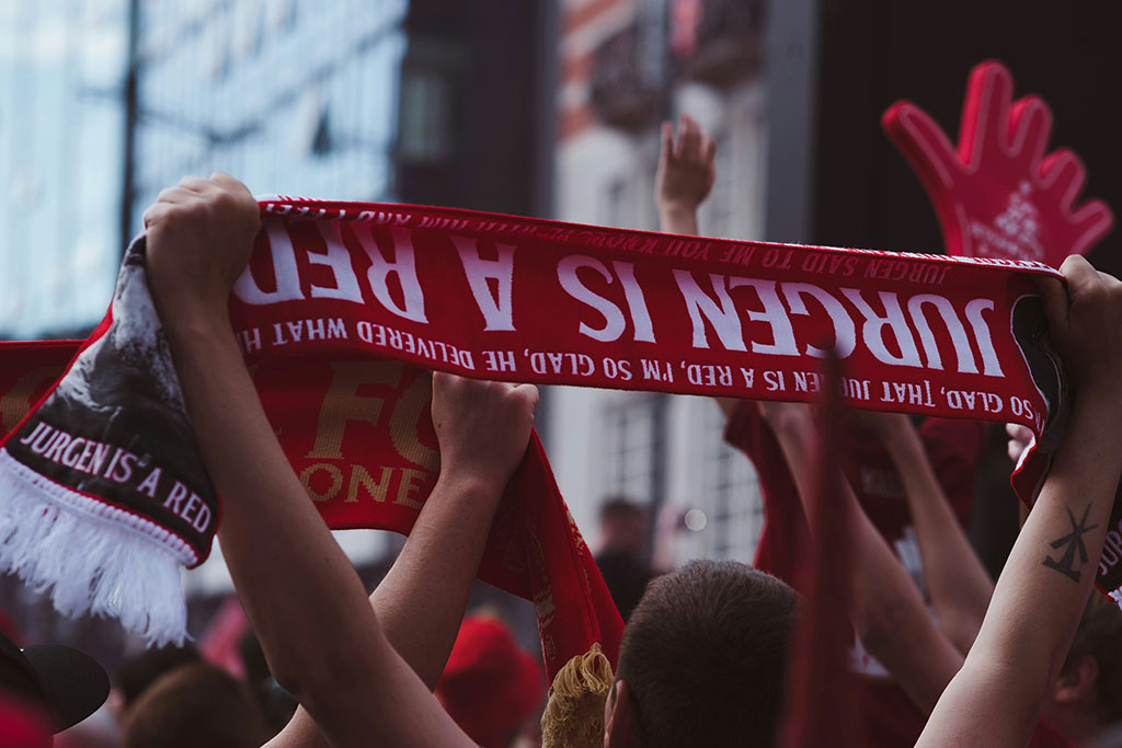 A fan holds an upside down football scrarf that reads 'Juergen is a red'.