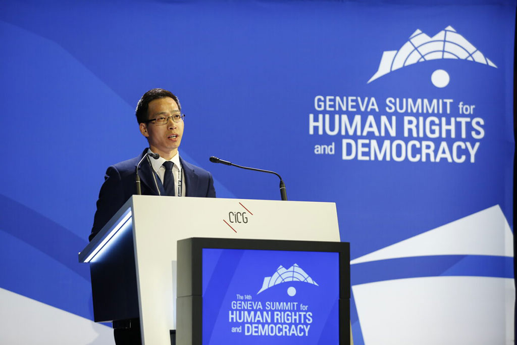 A conference speaker at a podium against a backdrop of blue.