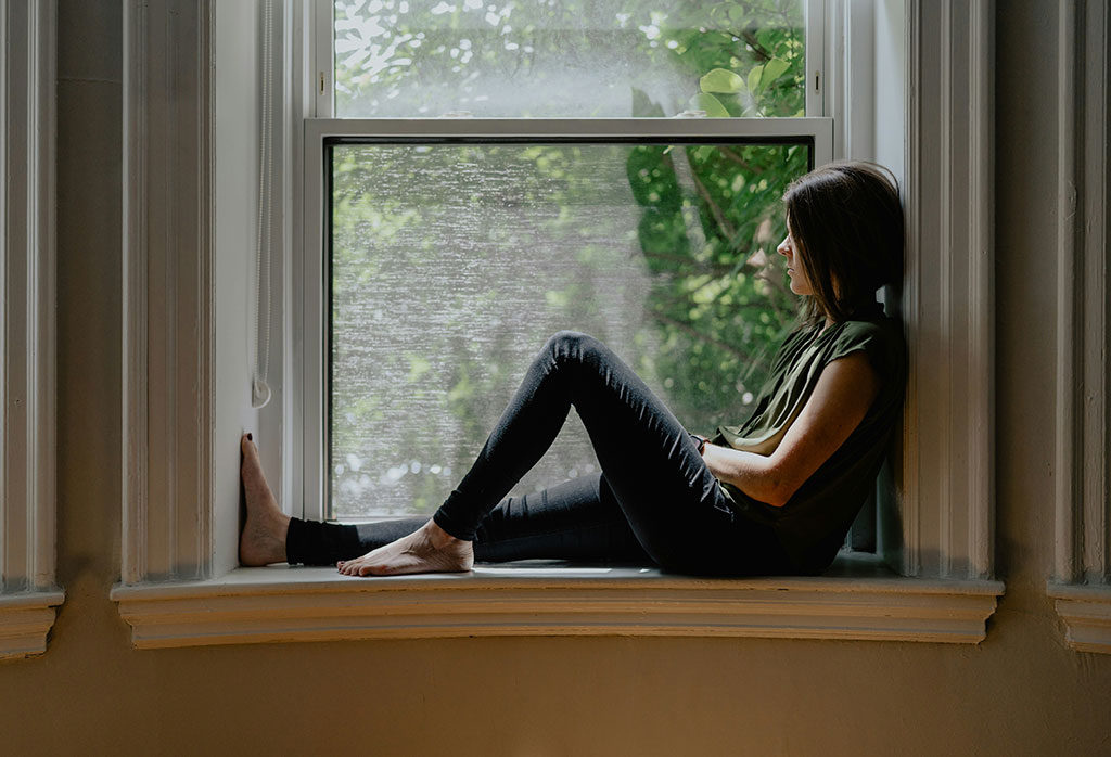 A person sits on a window sill with one raise knee.