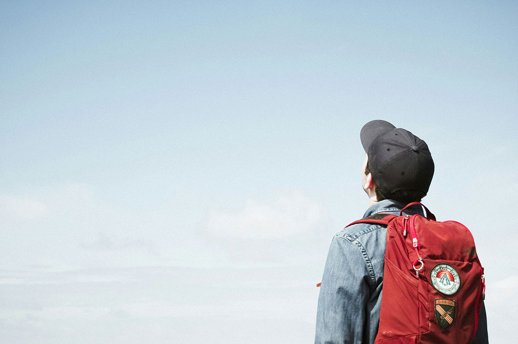 A person wearing a backpack looks to the sky.