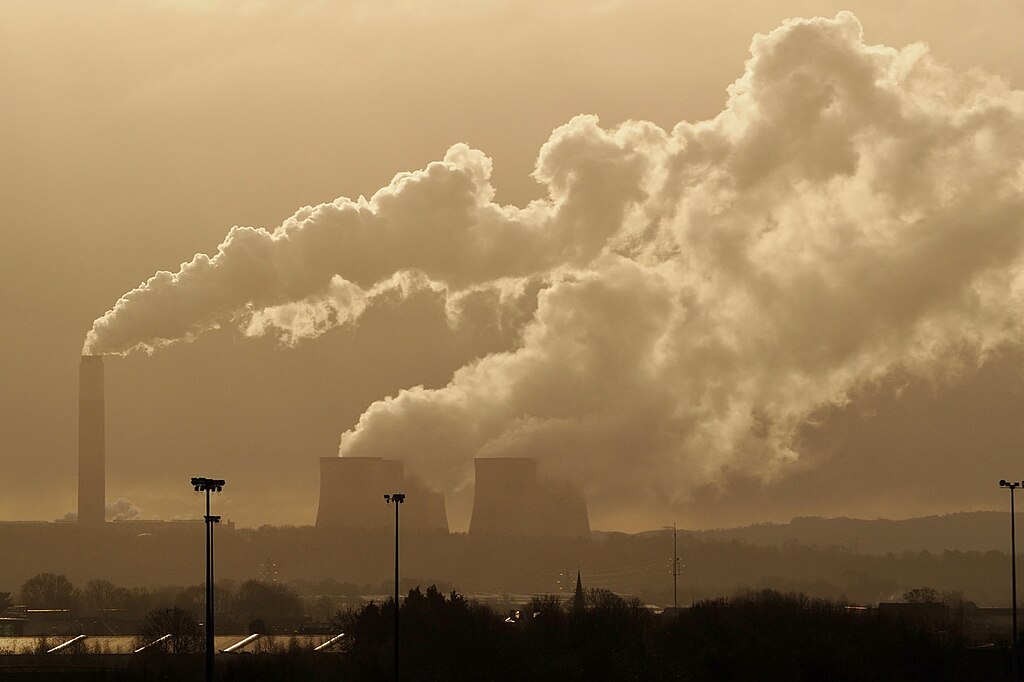 A sky line shows steam rising from a power station's chimney and cooling towers.