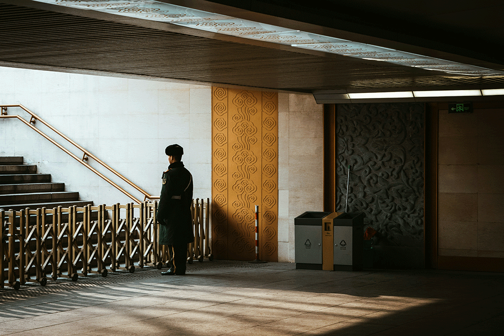 A guard stands behind a barrier across an entrance to a station escalator.