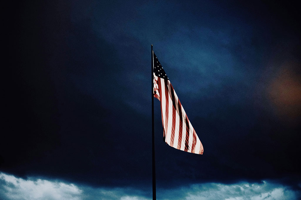 A US flag flutters under a dark brooding cloudy sky.