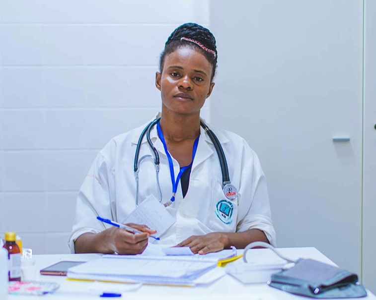 A tired-looking doctor sits at a desk dealing with paperwork.