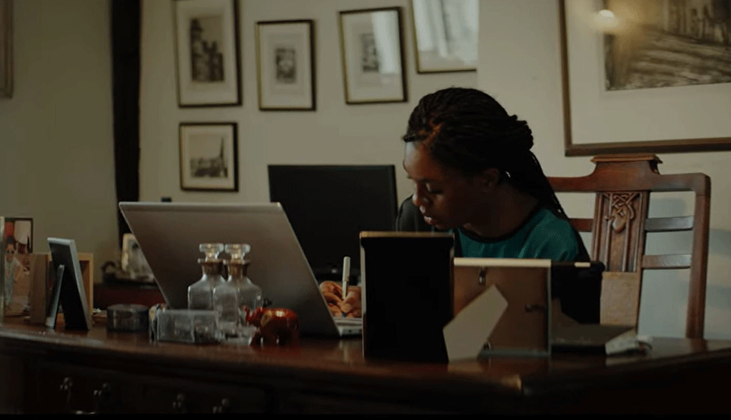A woman works at a laptop on a desk surrounded by picture frame.
