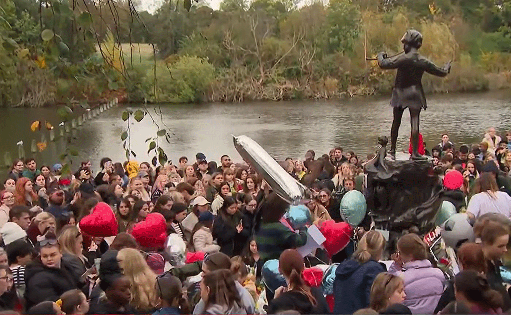 A crowd of teenagers gather by a Peter Pan statue to mourn a dead pop star