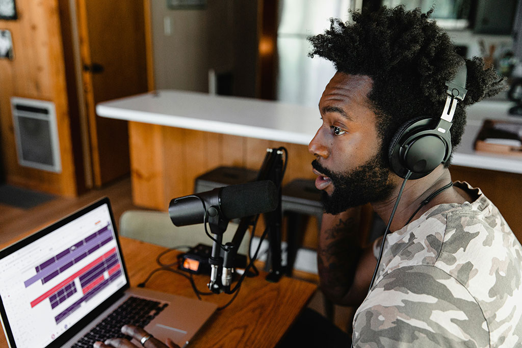 A podcaster speaks into a mic before a screen.
