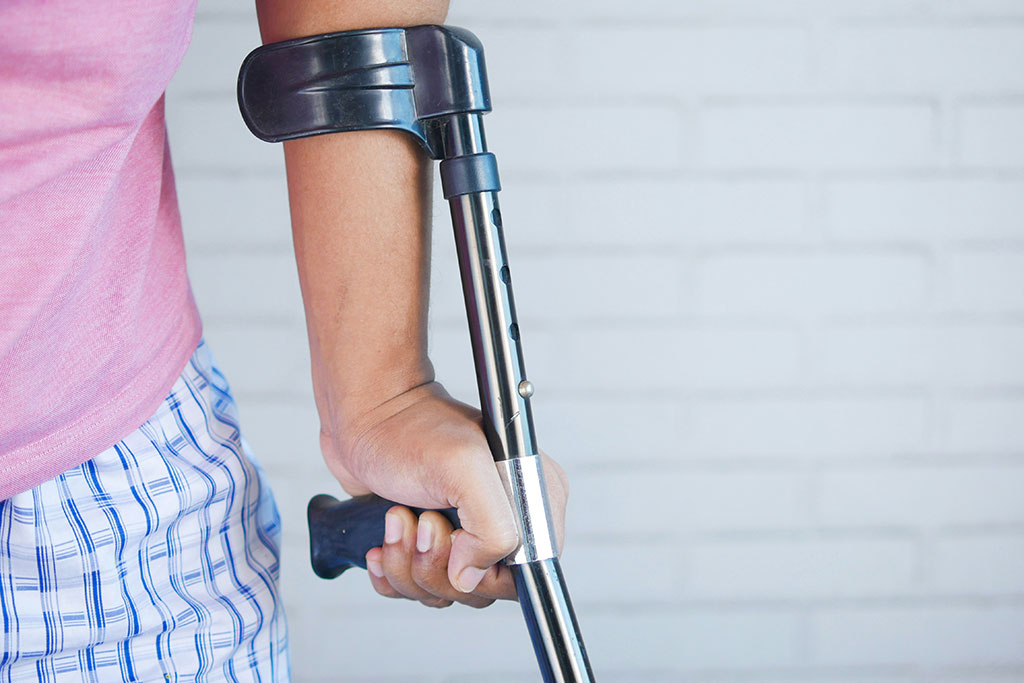 A crutch is held in the hand of someone in pyjamas.