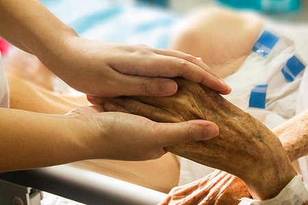 A younger hand holds a wrinkled older hand of someone in a bed.