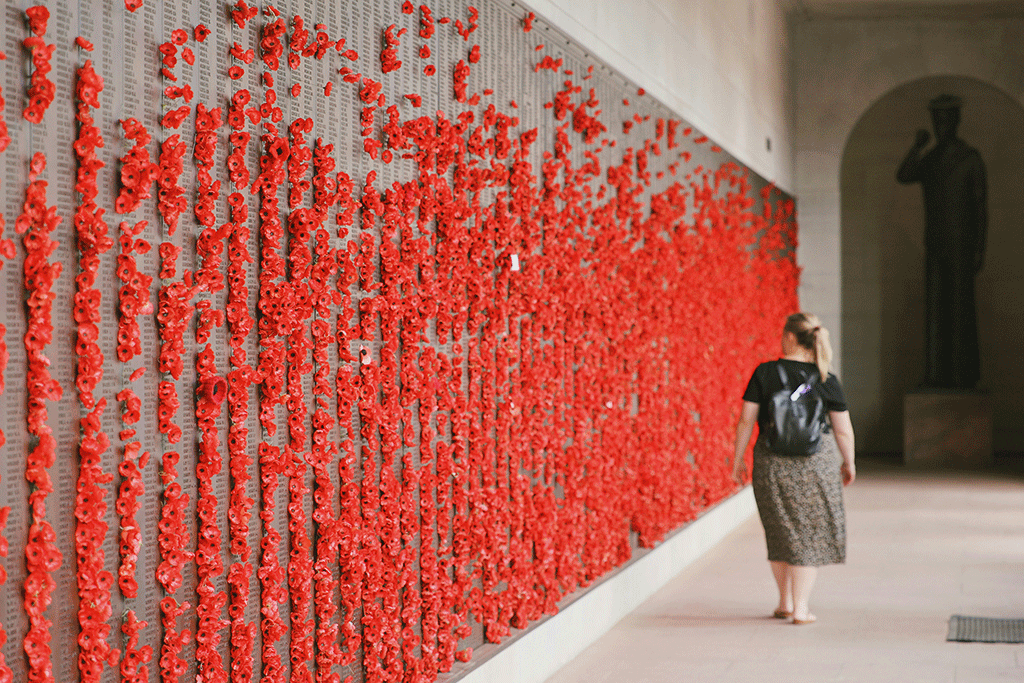 A woman walls along a war memorial wall covered in red poppies.