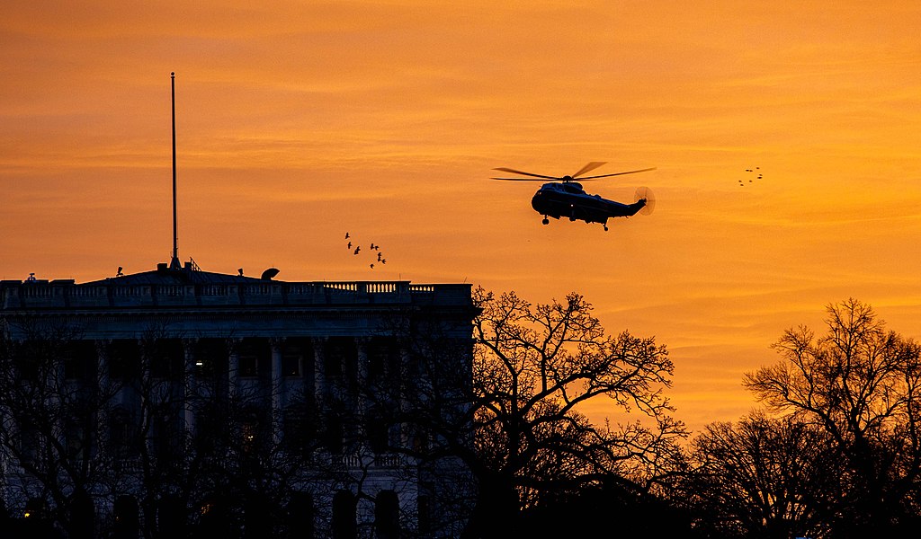 Silhoutted by a sun rise, a helicopter flies over The White House