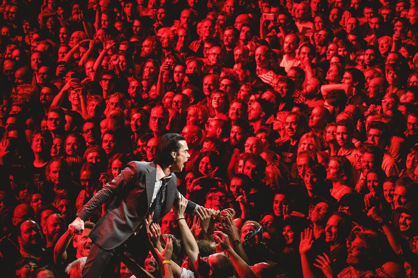 A rock star prowls the stage while behind hundred of faces tined red star.