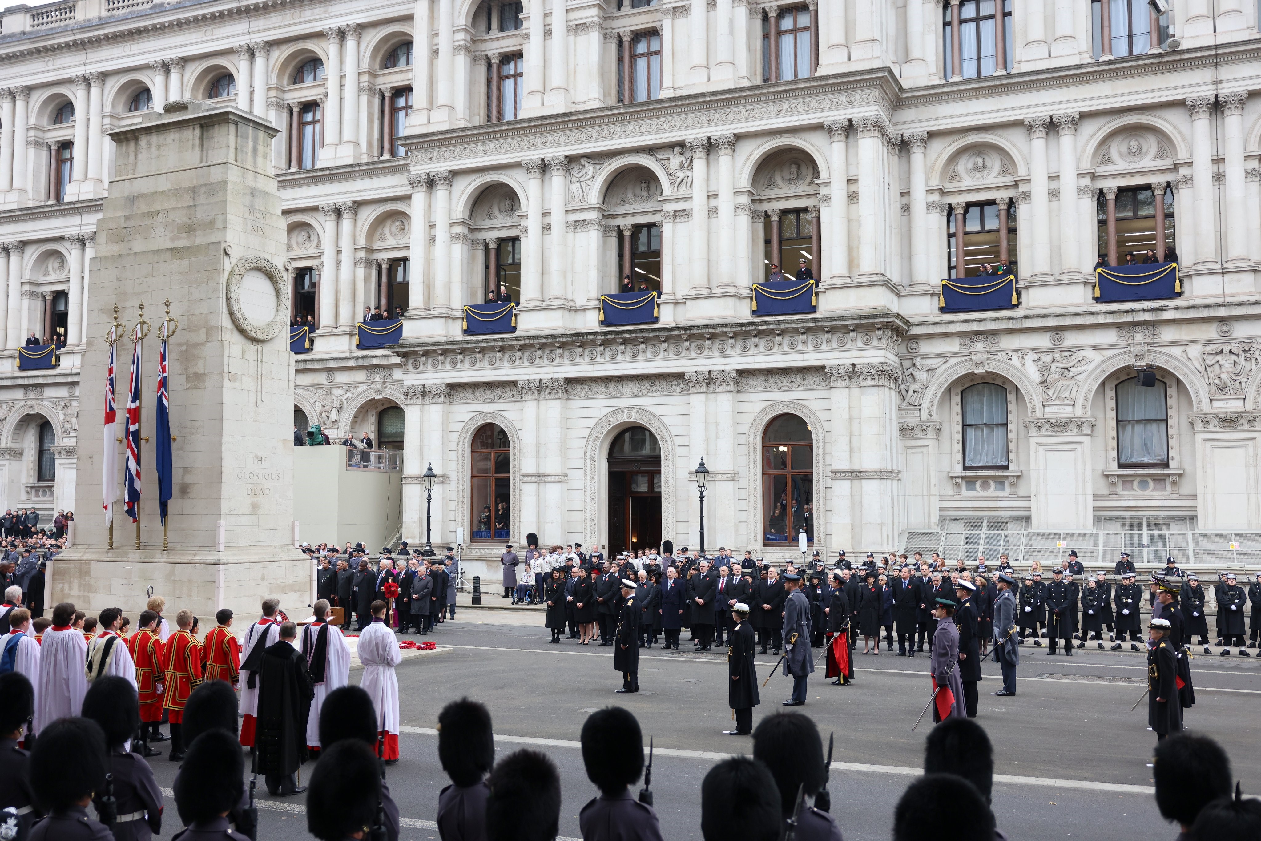 A Remembrance Sunday service stands to attention around a cenotaph.