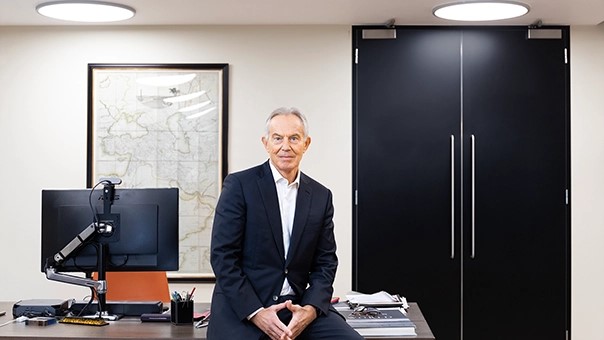 Tony Blair rests on the edge of a desk.