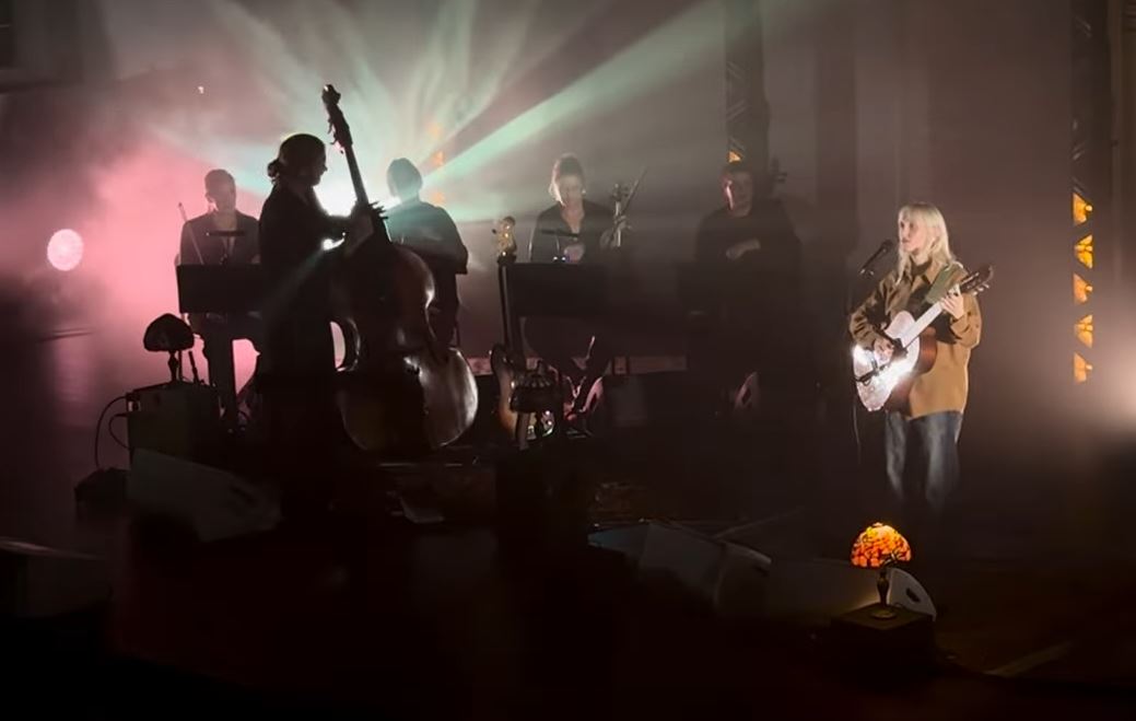 A misty back lit stage hosts a singing guitarist and a double base player