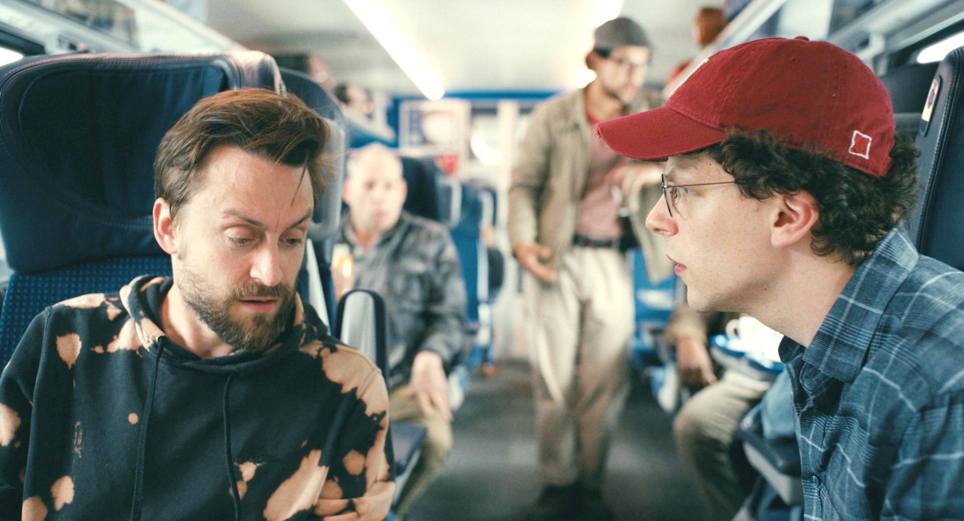 Two male cousins converse across the aisle of a train.