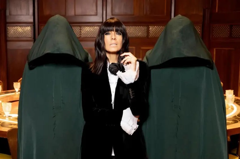 A TV show presenter looks imposing between two hooded figures.