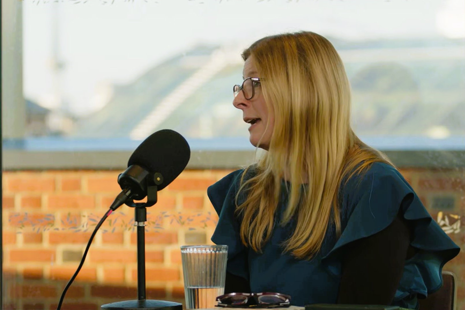 A woman sits at a table and talks with a microphone on a stand in front if her,