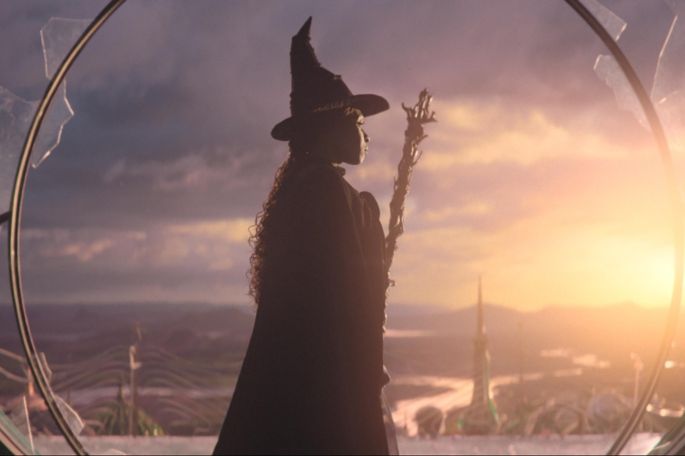 In a still from Wicked, the witch stands and looks to the sunset.