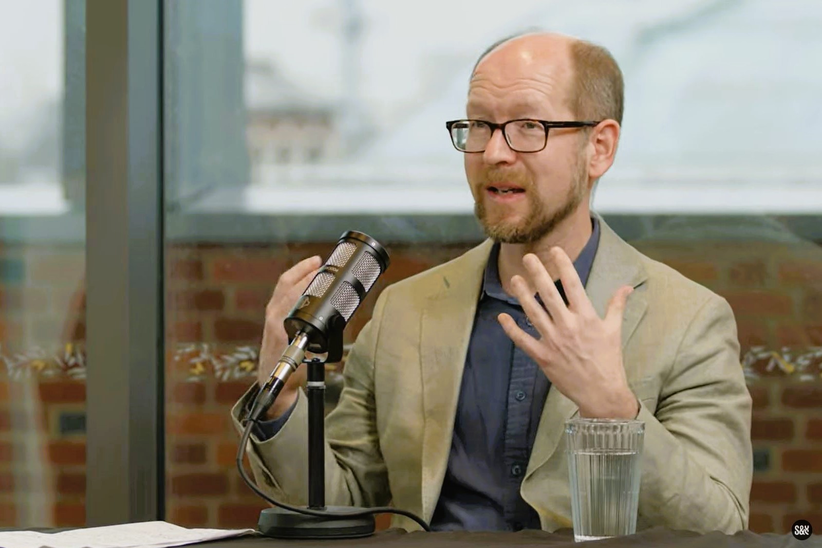 A podcast guest sits in front of a mic, gesturing with their hands.