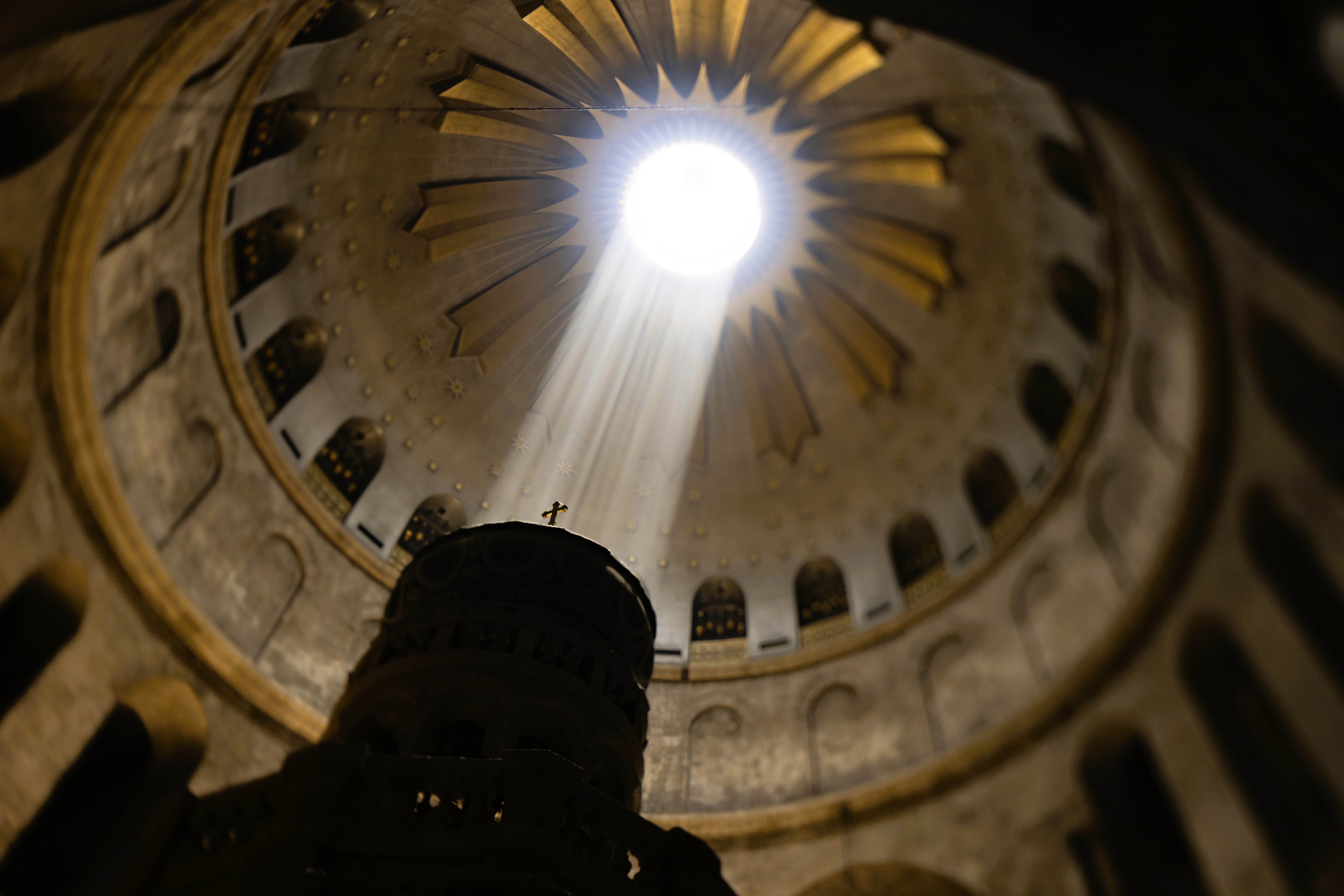 A shaft of light from an opening in a dome lights a cross on a pedestal.