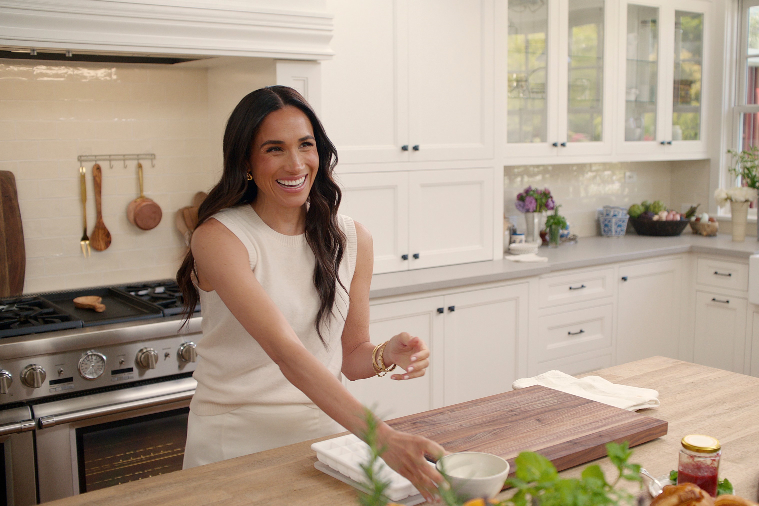A woman stands at a kitchen island with a chopping board on it.