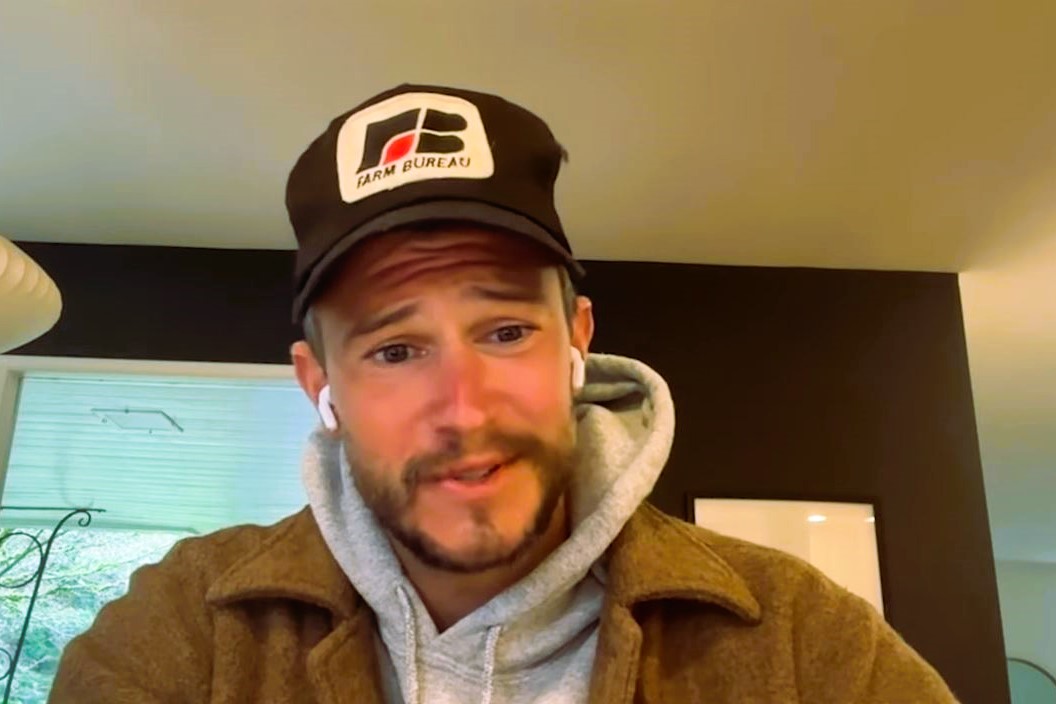 A podcast guest, wearing a baseball hat, looks at a screen.