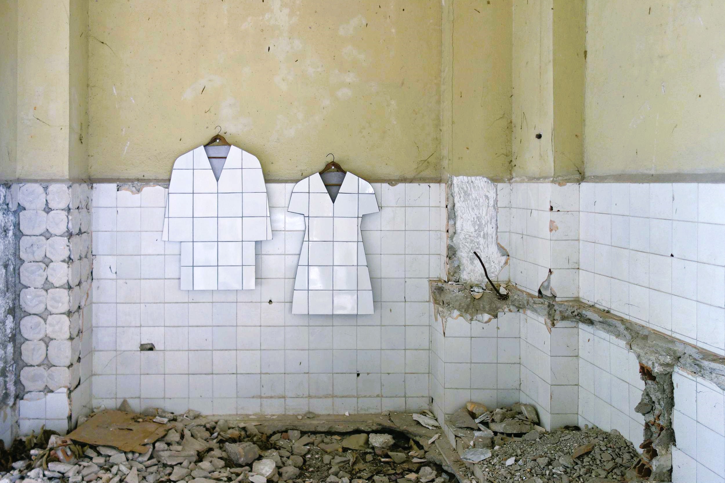 In a bombed-out tiled room, two art works hang in the shape of a tiled jacket and shape
