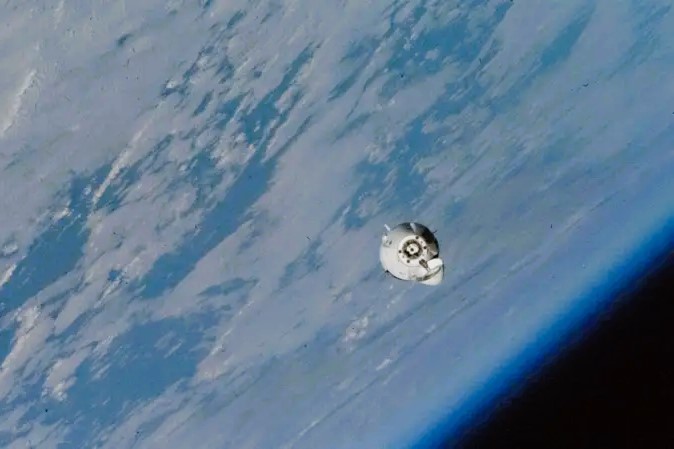 A small white space capsule orbits around the earth.
