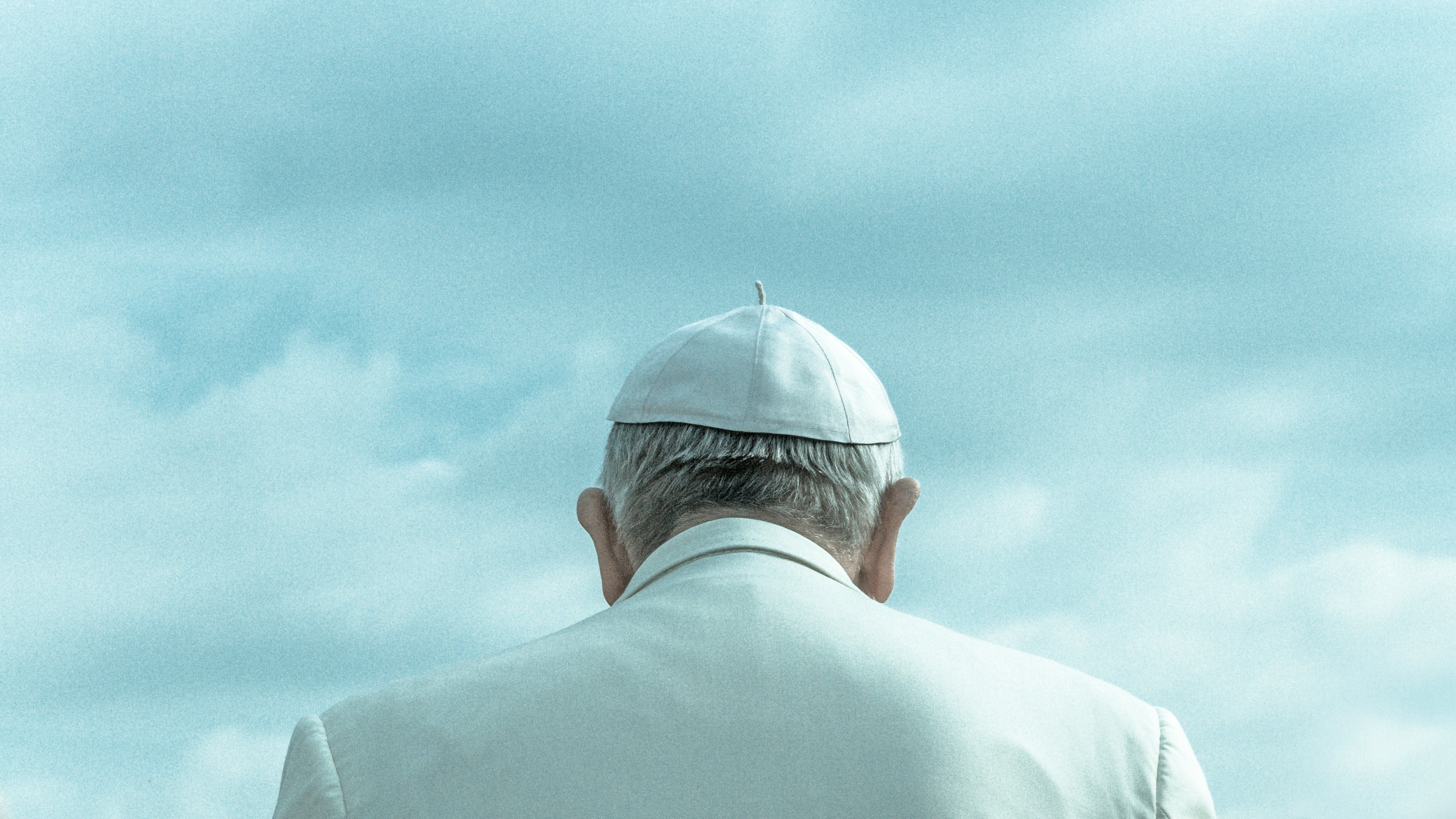 A pope wearing a white skull cap and white robe, viewed from behind