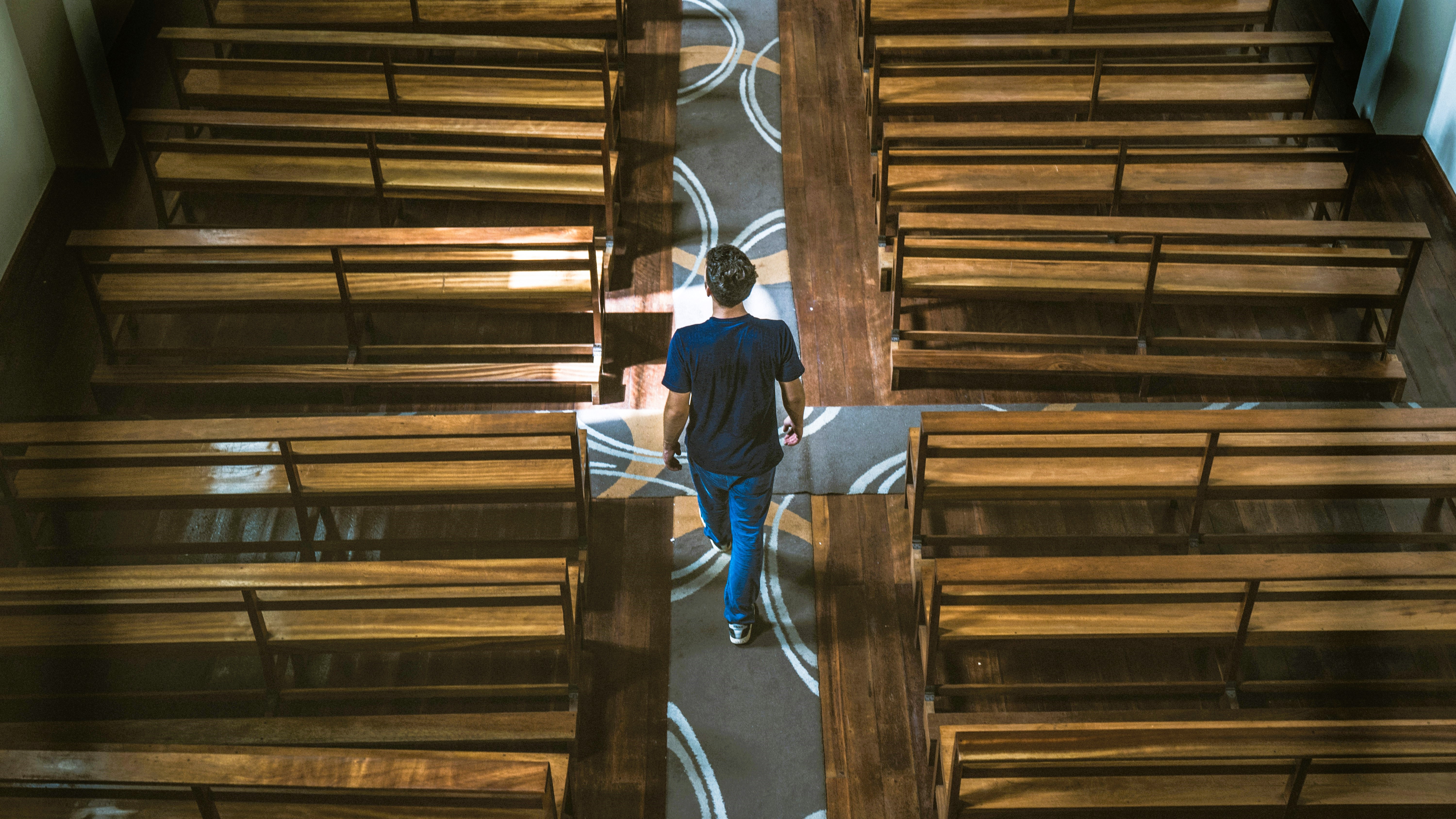 A casually dressed man strides down the aisle of a church between the pews.
