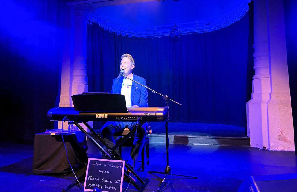 A pianist sits at a keyboard singing on a stage.
