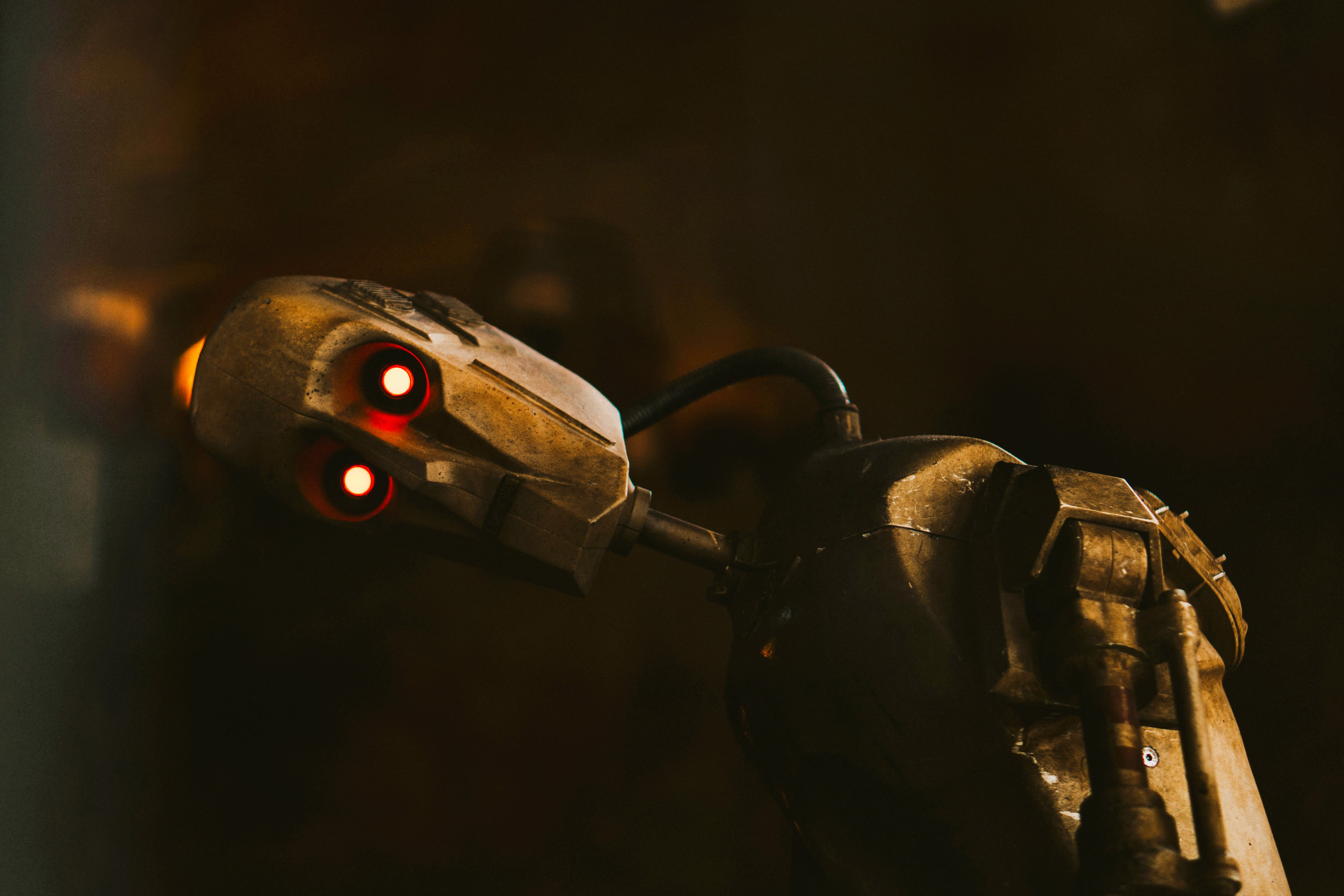 A tarnished humaniod robot rests its head to the side, its LED eyes look to the camera.