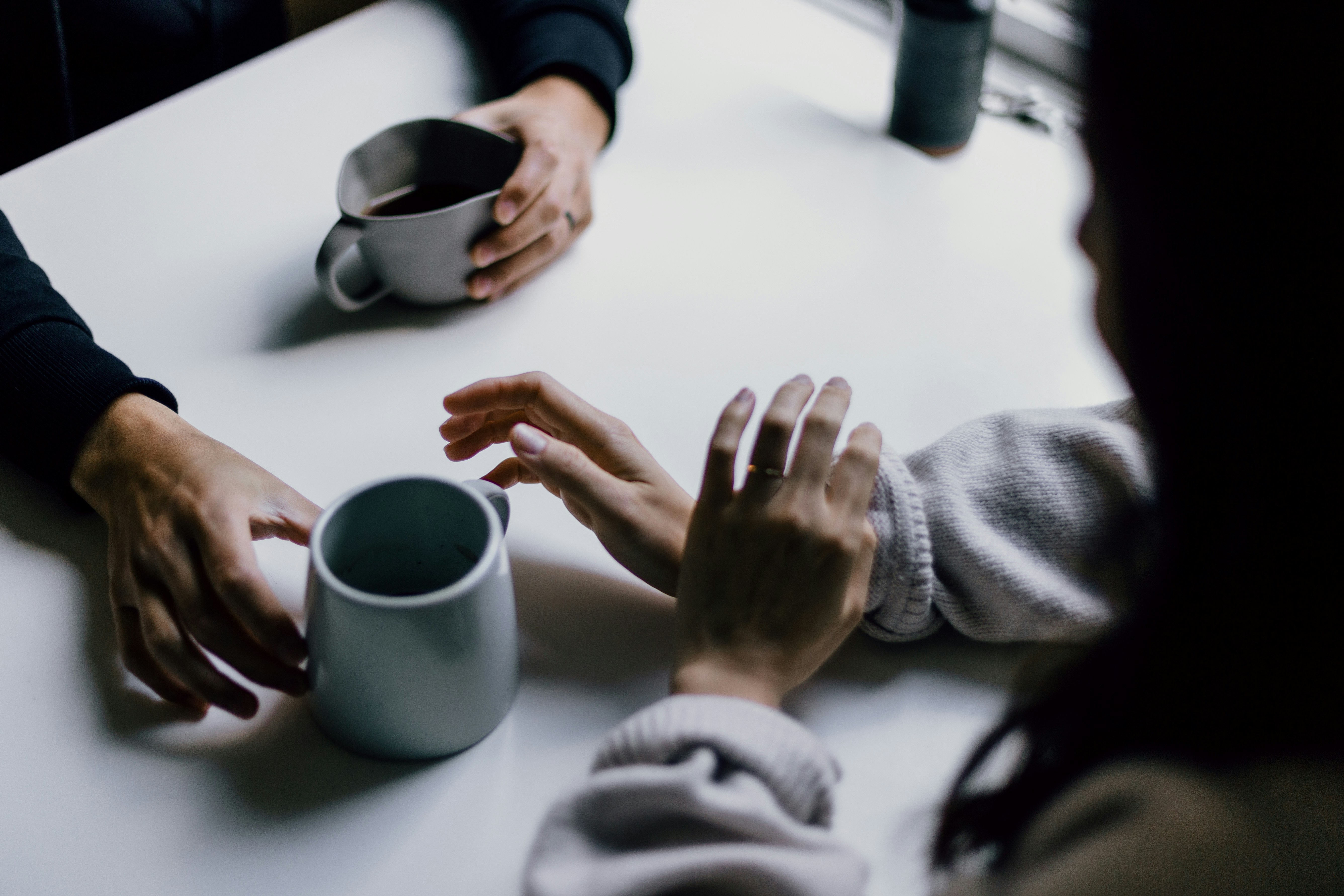 A cup of coffee is offered across a table to a hand that is hesitant.