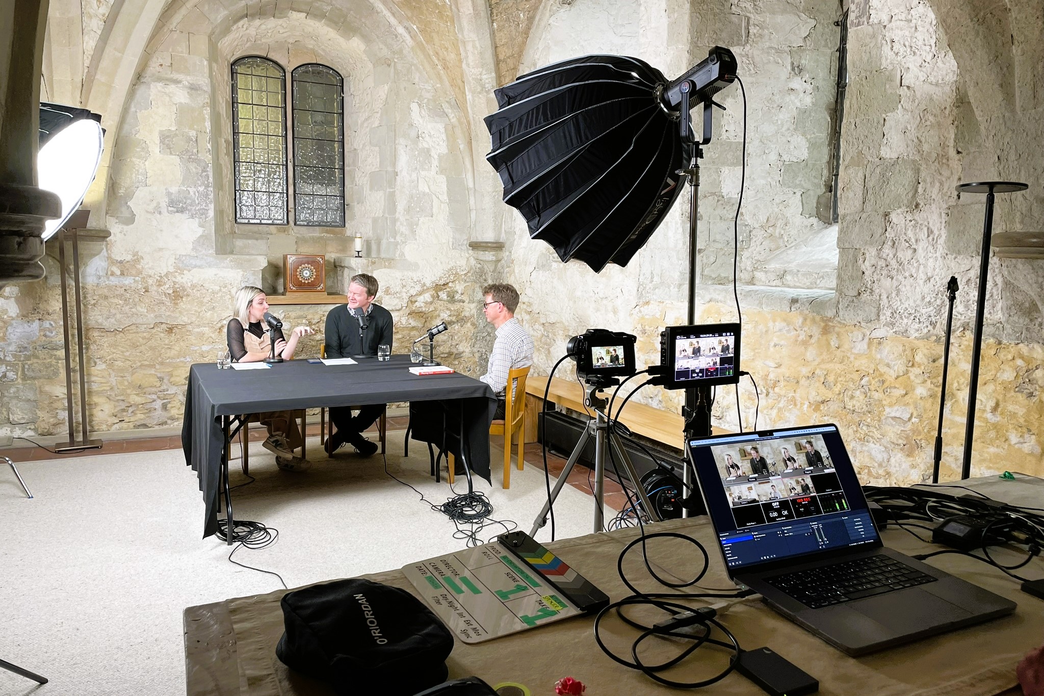 A podcast recording showing a table with guest and a table with equipment.