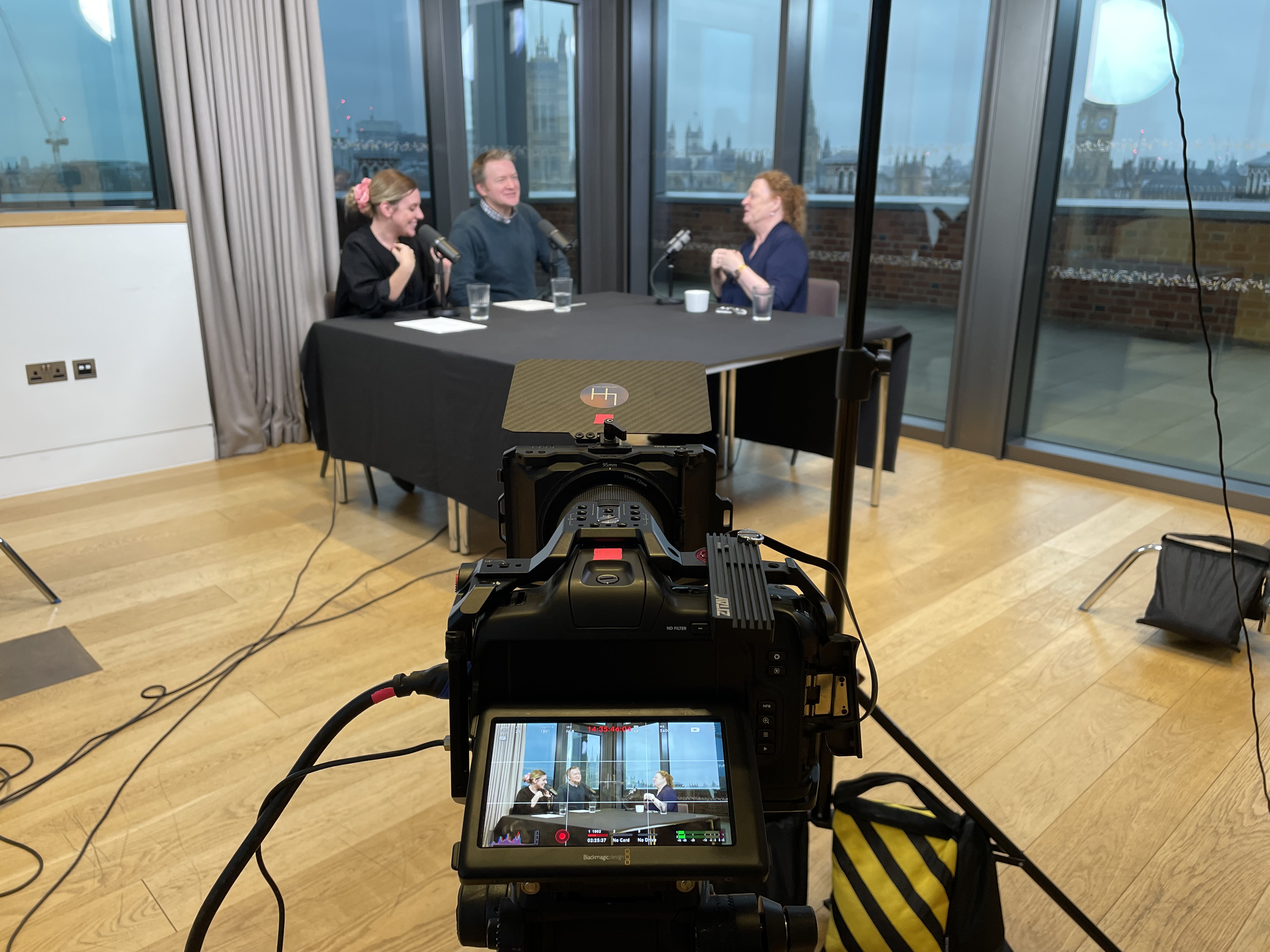 A camera's screen shows a podcast recording also visible in the background.
