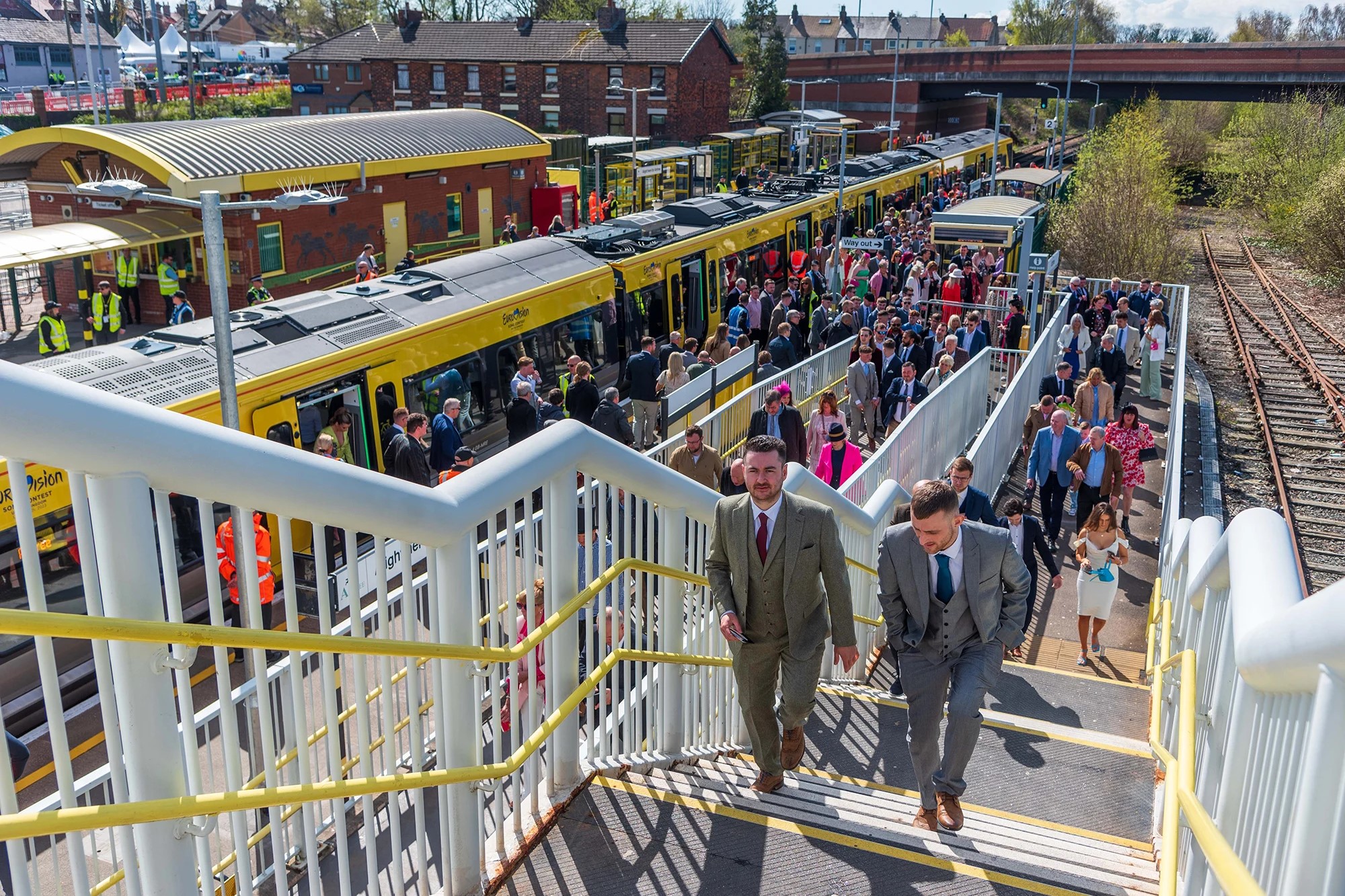 Smartly dressed people crowd a station platform and stairs.